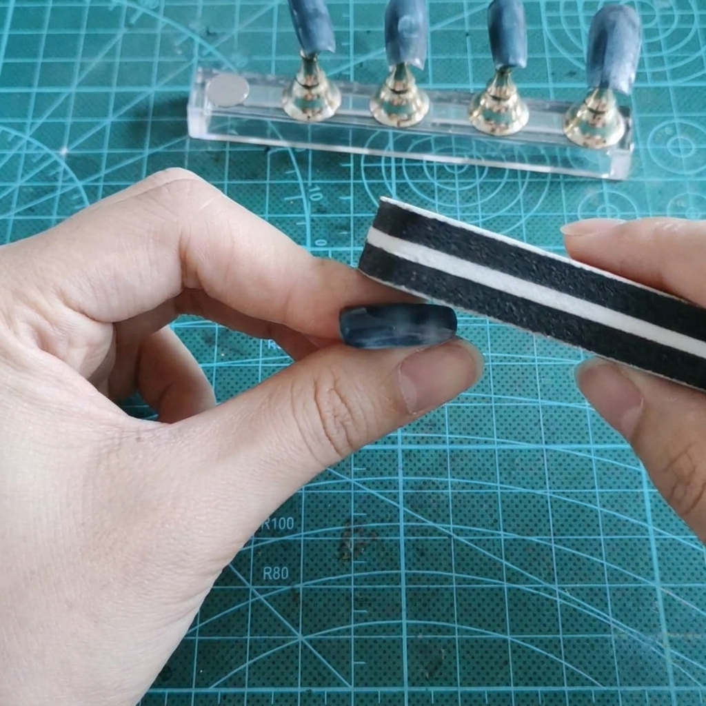 Un mattoncino buffer leviga la superficie lucida in gel di ununghia finta tenuta tra le dita.
