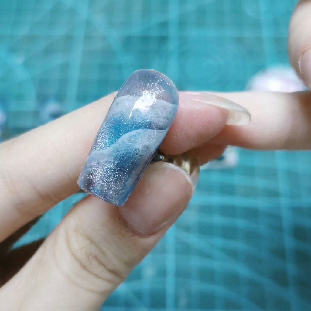 Una vista ravvicinata di una singola unghia ricoperta da scintillanti glitter olografici incastonati in gel trasparente.
