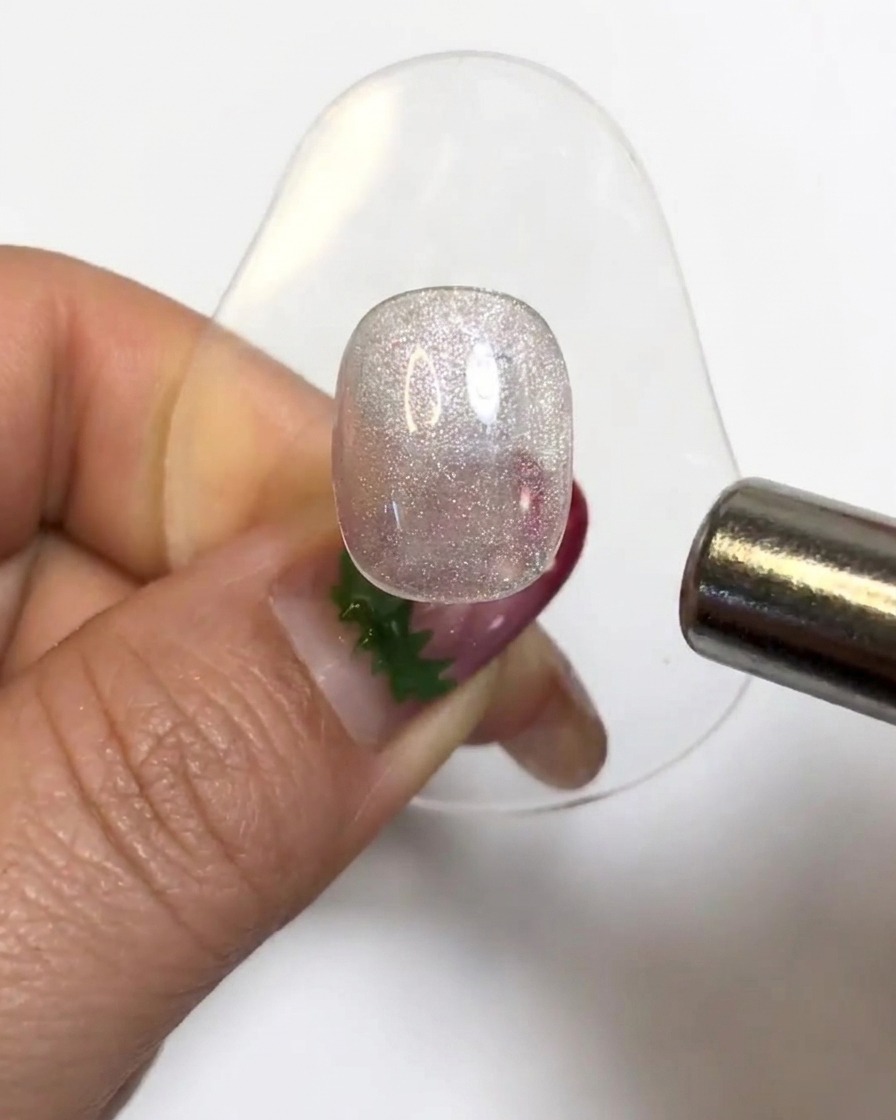 Un magnete cilindrico che fluttua sopra una tip di unghia in gel brillante per attivare le particelle cat-eye.