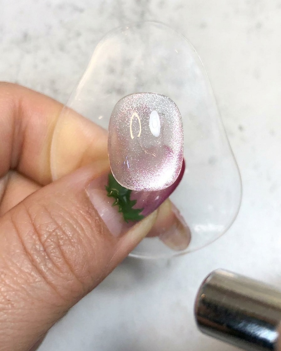 Una lampada UV portatile che illumina ununghia in gel magnetico brillante su un supporto per polimerizzarla.