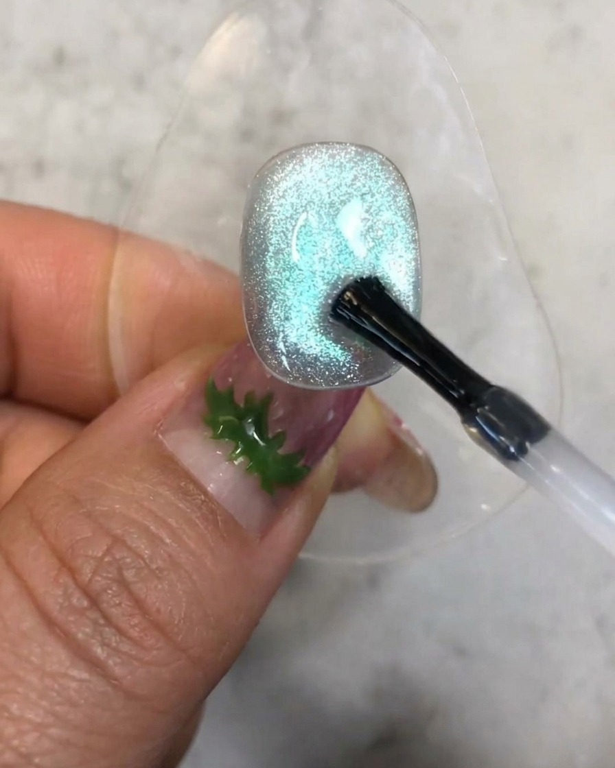 Un pennello che applica una piccola goccia di gel rinforzante trasparente sulla superficie testurizzata dellunghia blu cat-eye.