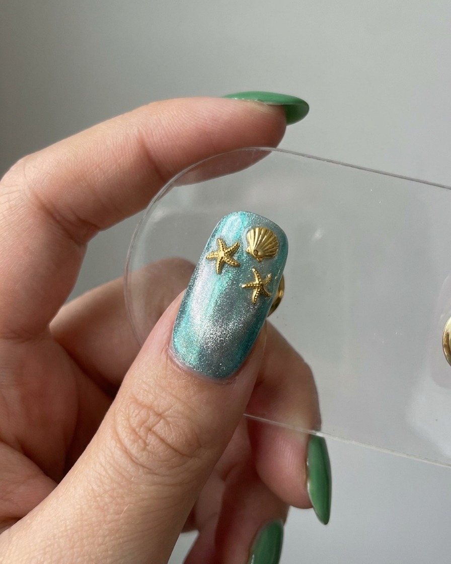 Unanteprima dellunghia finita che mostra una base blu cat-eye decorata con charm dorati a forma di stella marina e conchiglia.
