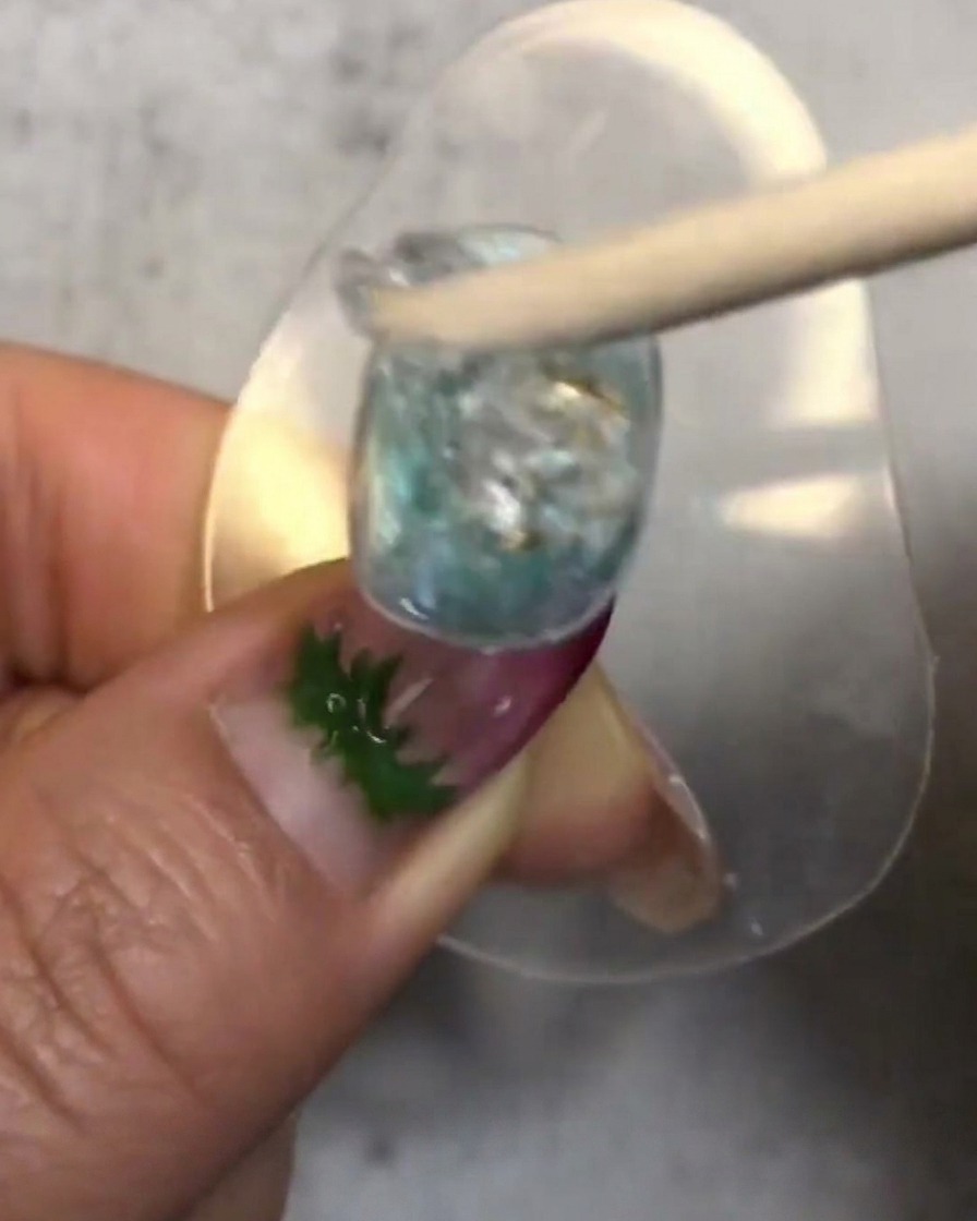 Un bastoncino di legno che mescola e posiziona una pallina di soft candy gel traslucido sullunghia decorata.