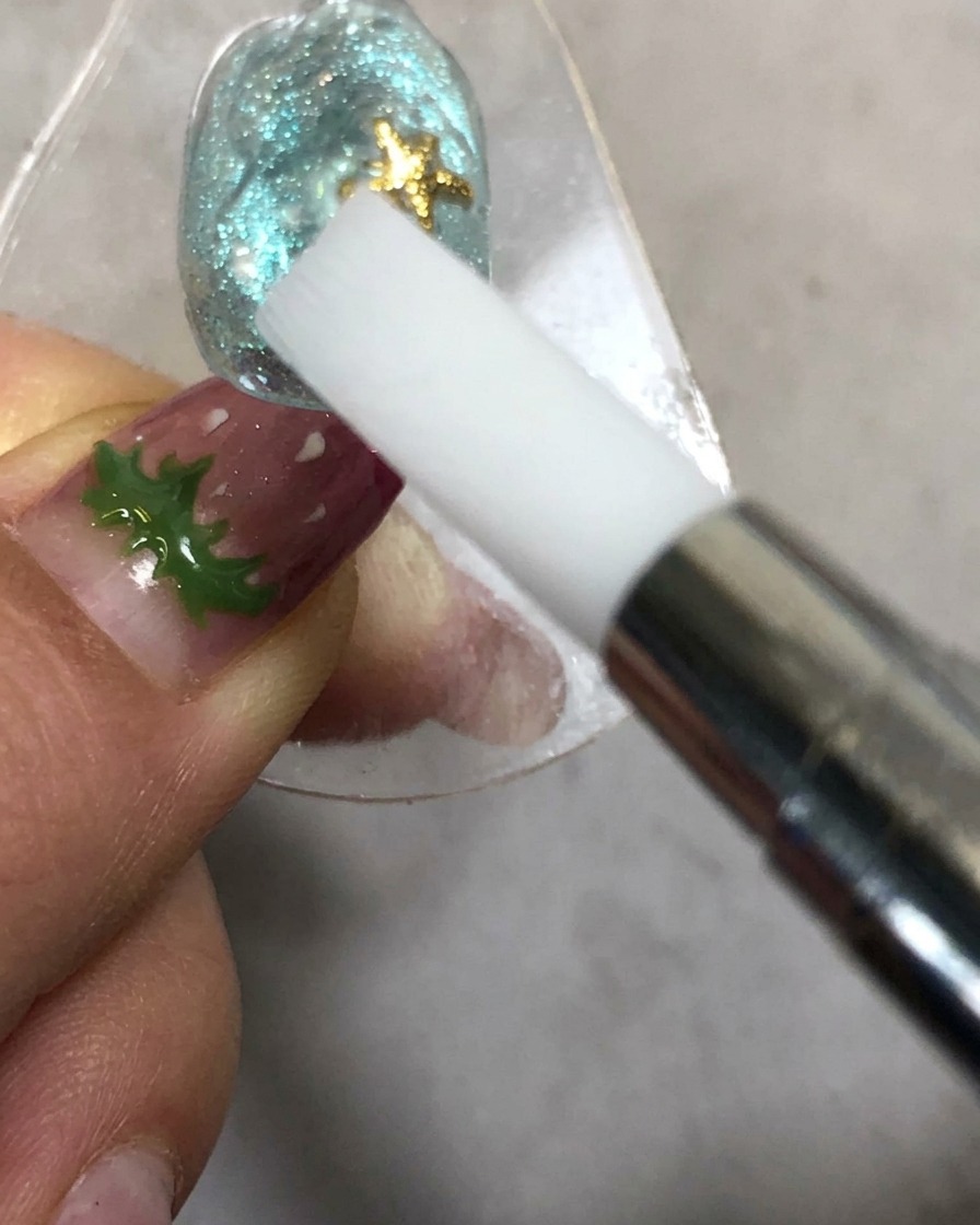 Una mano che tiene uno strumento di modellatura in silicone vicino a ununghia sotto una lampada di polimerizzazione.