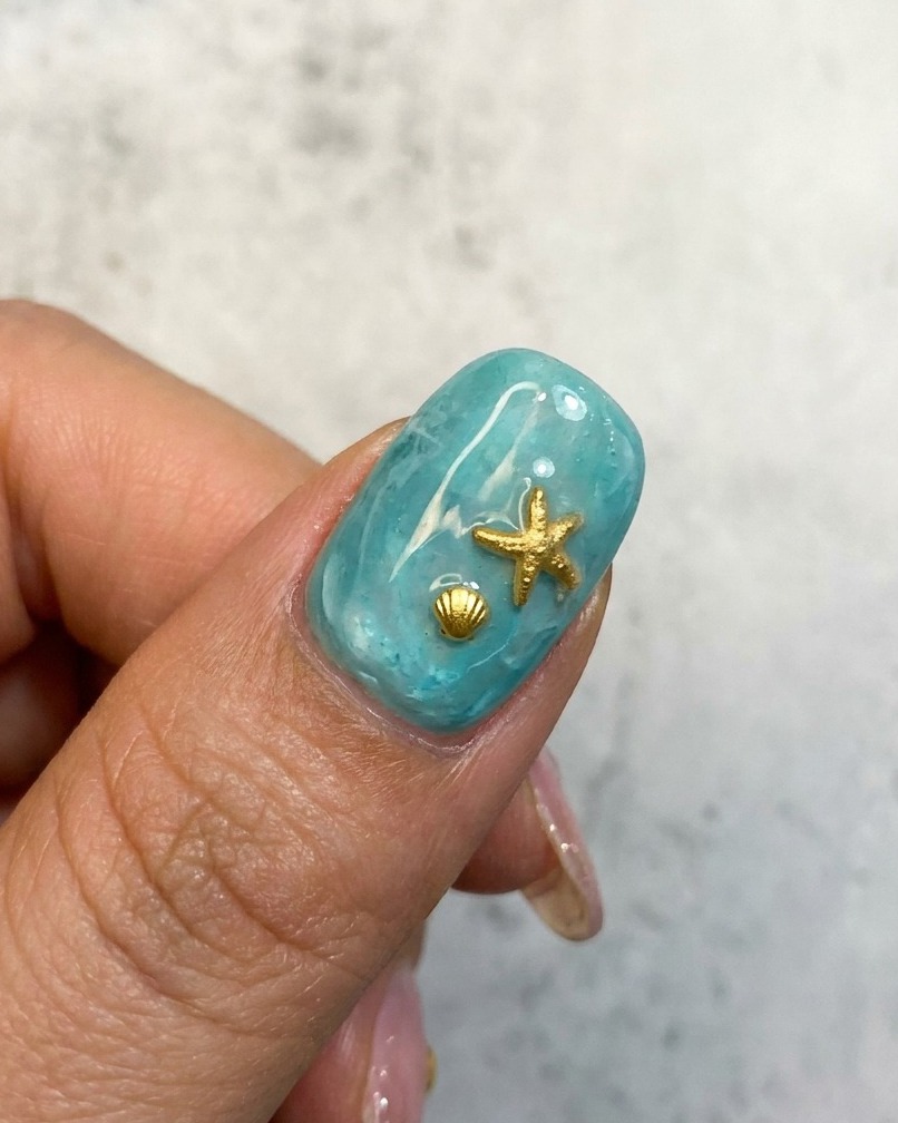 Un primo piano di un design per unghie oceaniche blu con una stella marina dorata e un abbellimento a conchiglia.