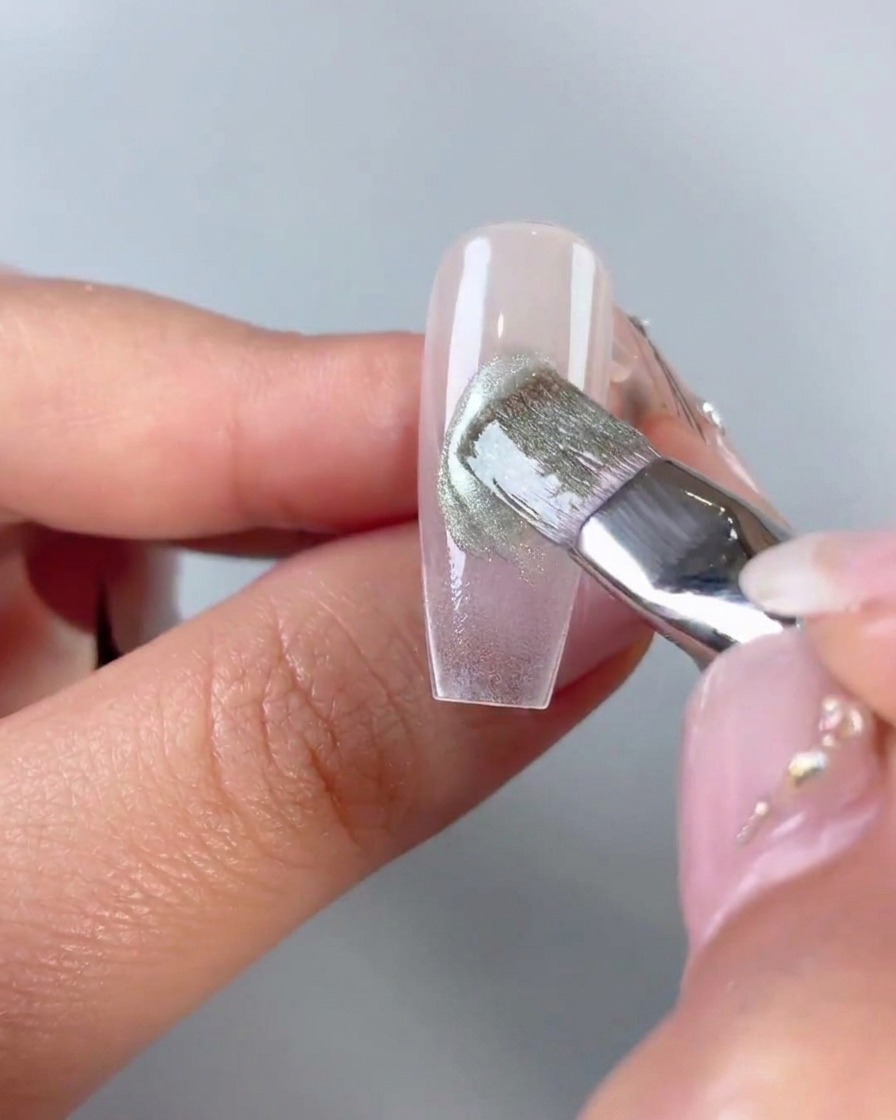 Un pennello piatto che livella e sfuma il gel cat-eye verde applicato in diagonale al centro di una tip trasparente.