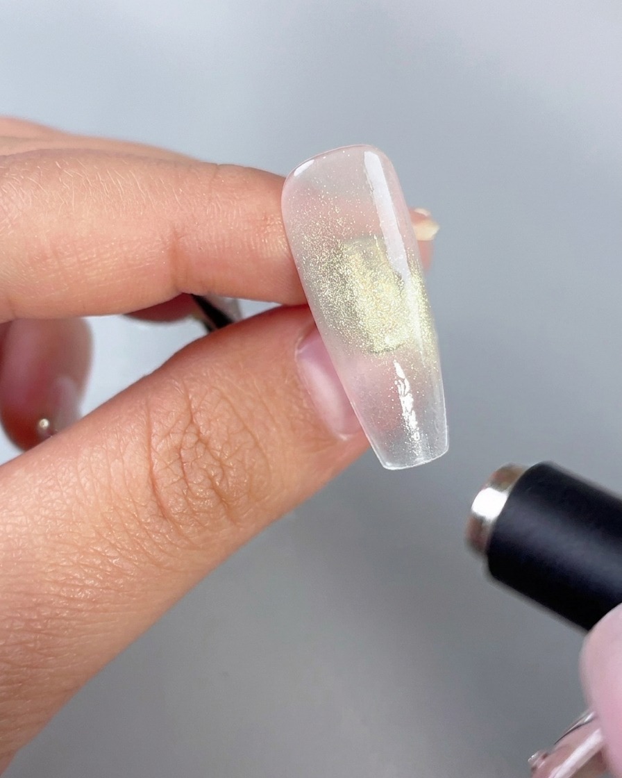 Un magnete cilindrico tenuto vicino a ununghia lucida in gel verde per attivare leffetto cat-eye.