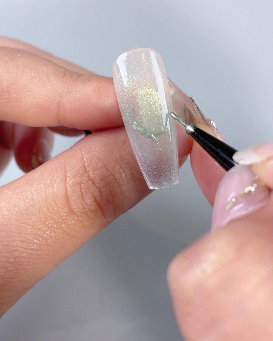 Un pennello fine per nail art che disegna i contorni delle ali di farfalla su una tip ungueale.
