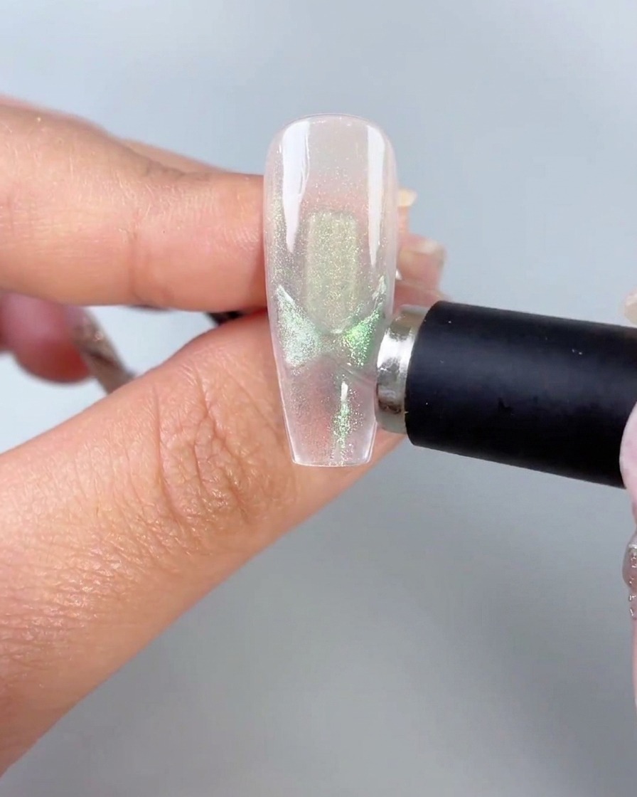 Una bacchetta magnetica nera tenuta vicino al lato di una tip trasparente che mostra motivi di ali di farfalla cat-eye verdi attivati.