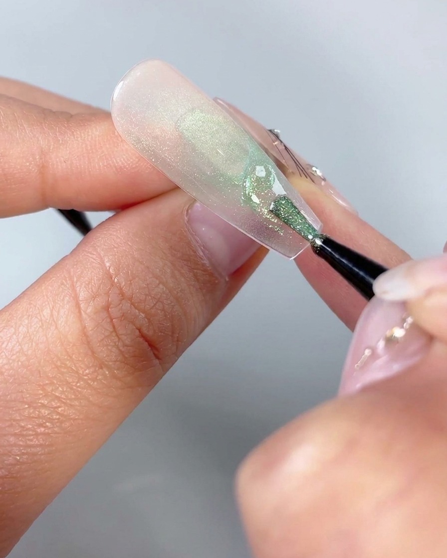 Un pennello fine per nail art che disegna piccole forme triangolari curve vicino alla base inferiore di un design per unghie con farfalle.