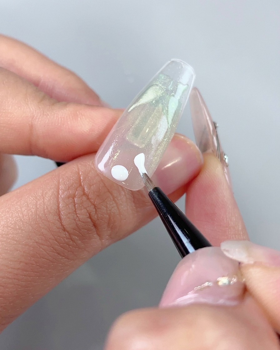 Un pennello darte fine che applica punti in gel bianco e tratti iniziali vicino allarea delle cuticole di ununghia.