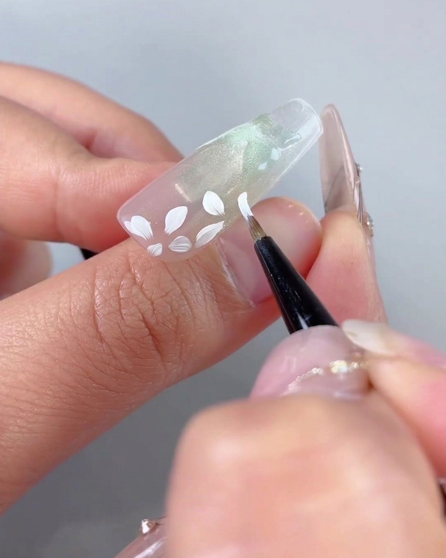 Un pennello darte fine che aggiunge piccoli dettagli di petali bianchi attorno alla grande base floreale dipinta in precedenza.