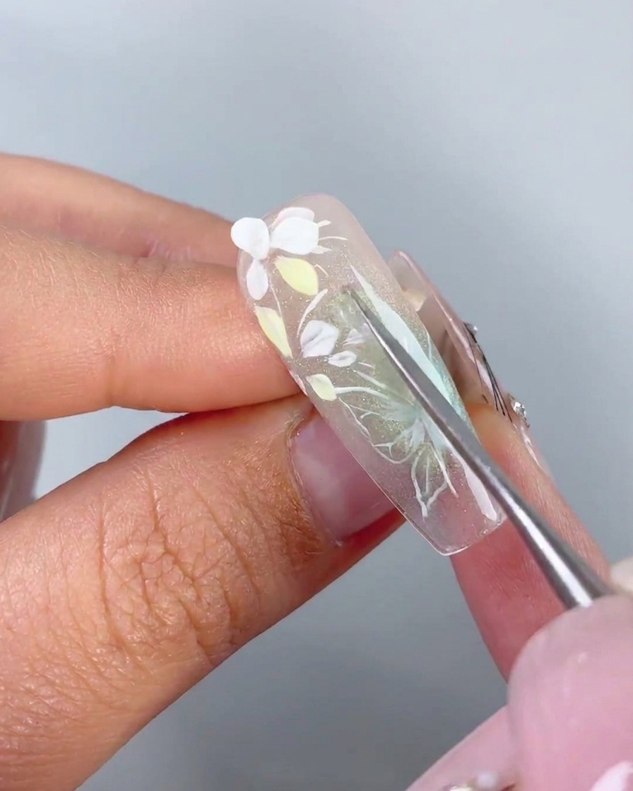 Uno strumento di metallo che posiziona un petalo 3D bianco preformato sul gel adesivo di ununghia.