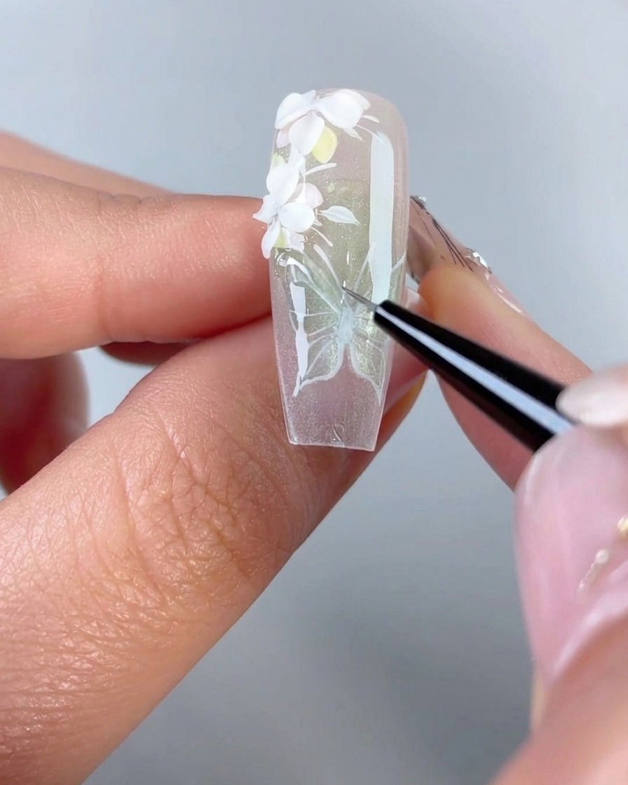 Primo piano di un pennello liner fine che traccia gel modellante trasparente 3D sulle linee bianche dipinte di un design ad ala di farfalla su una tip in gel.
