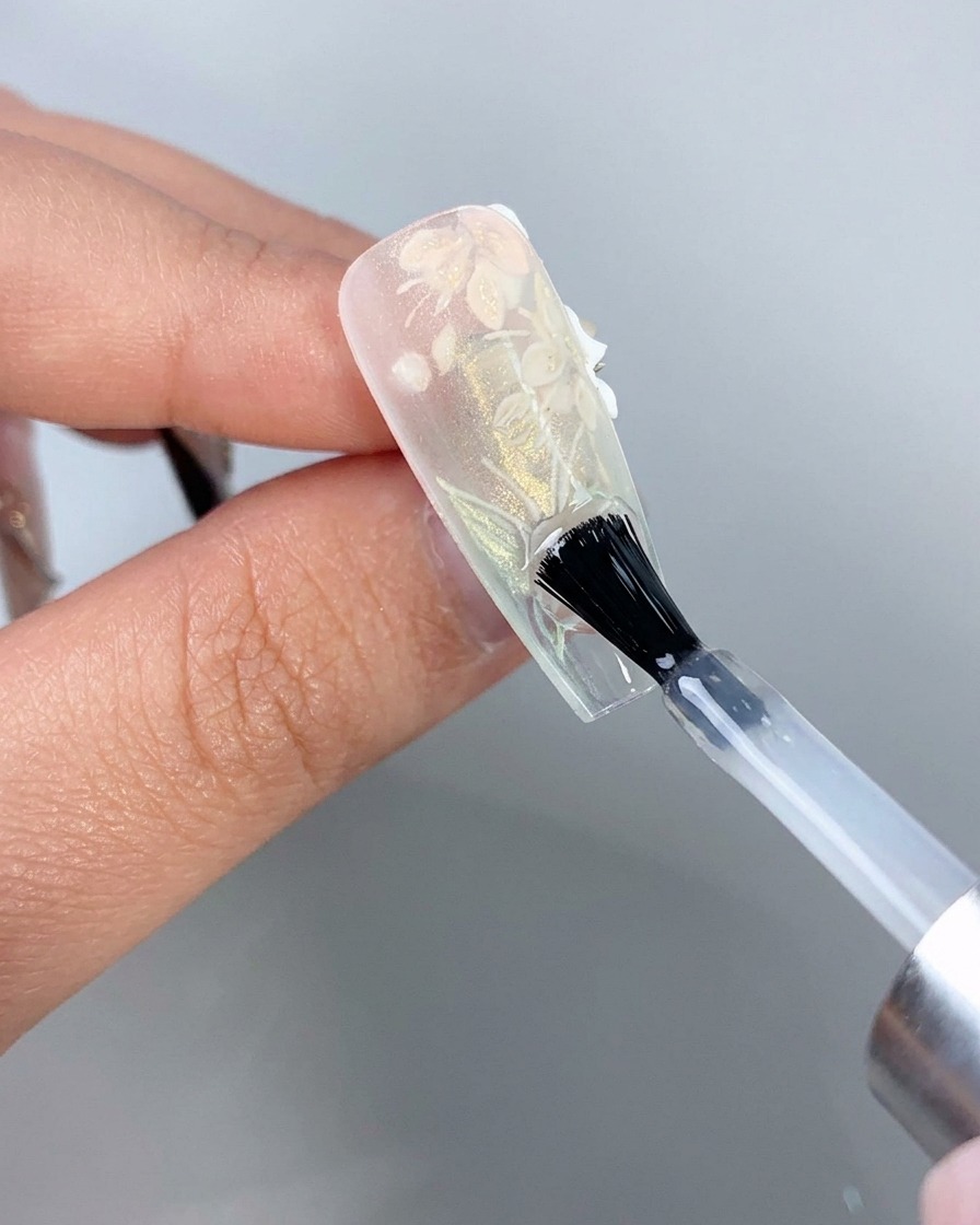 Un pennello per unghie che applica un top coat trasparente sulla parte inferiore del bordo libero di una tip di unghia con estensione trasparente.