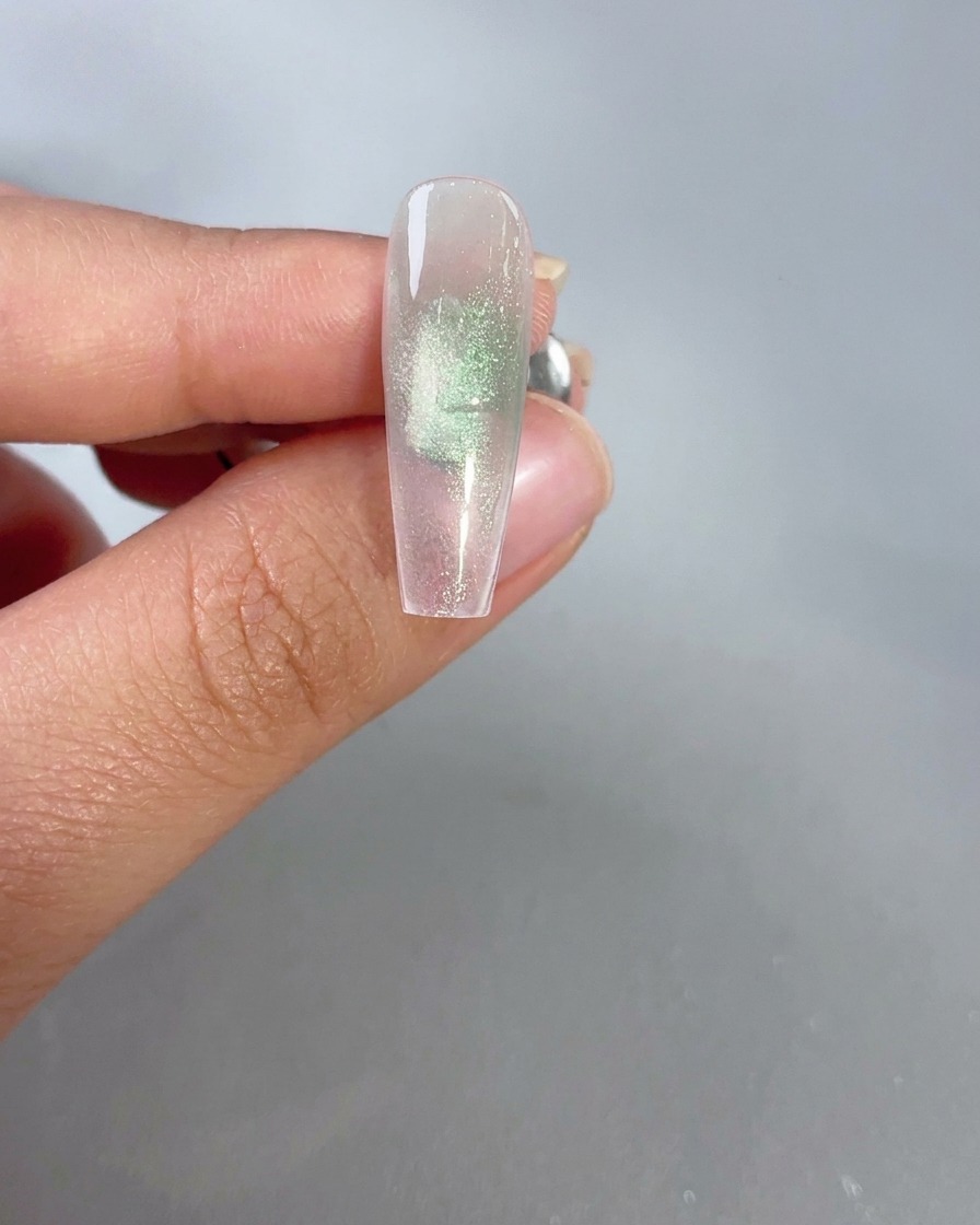 Un magnete tenuto vicino a ununghia in gel cat-eye verde trasparente per attivare leffetto brillante.