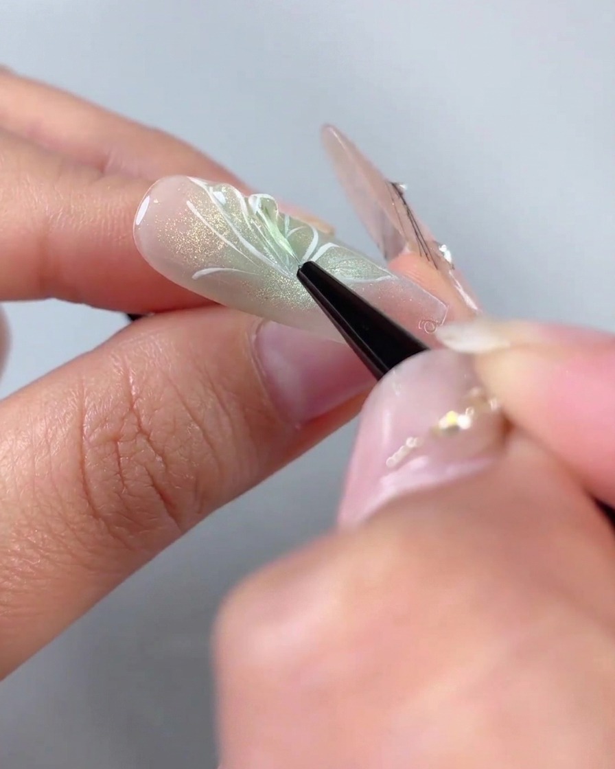 Un pennello liner fine che applica gel modellante trasparente 3D sui contorni delle ali dipinte di bianco di un design per unghie a mezza farfalla.