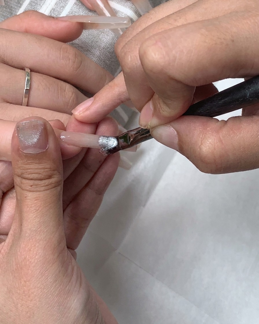 Un pennello piatto per gel applica il gel cat-eye argentato su tutta lunghia.