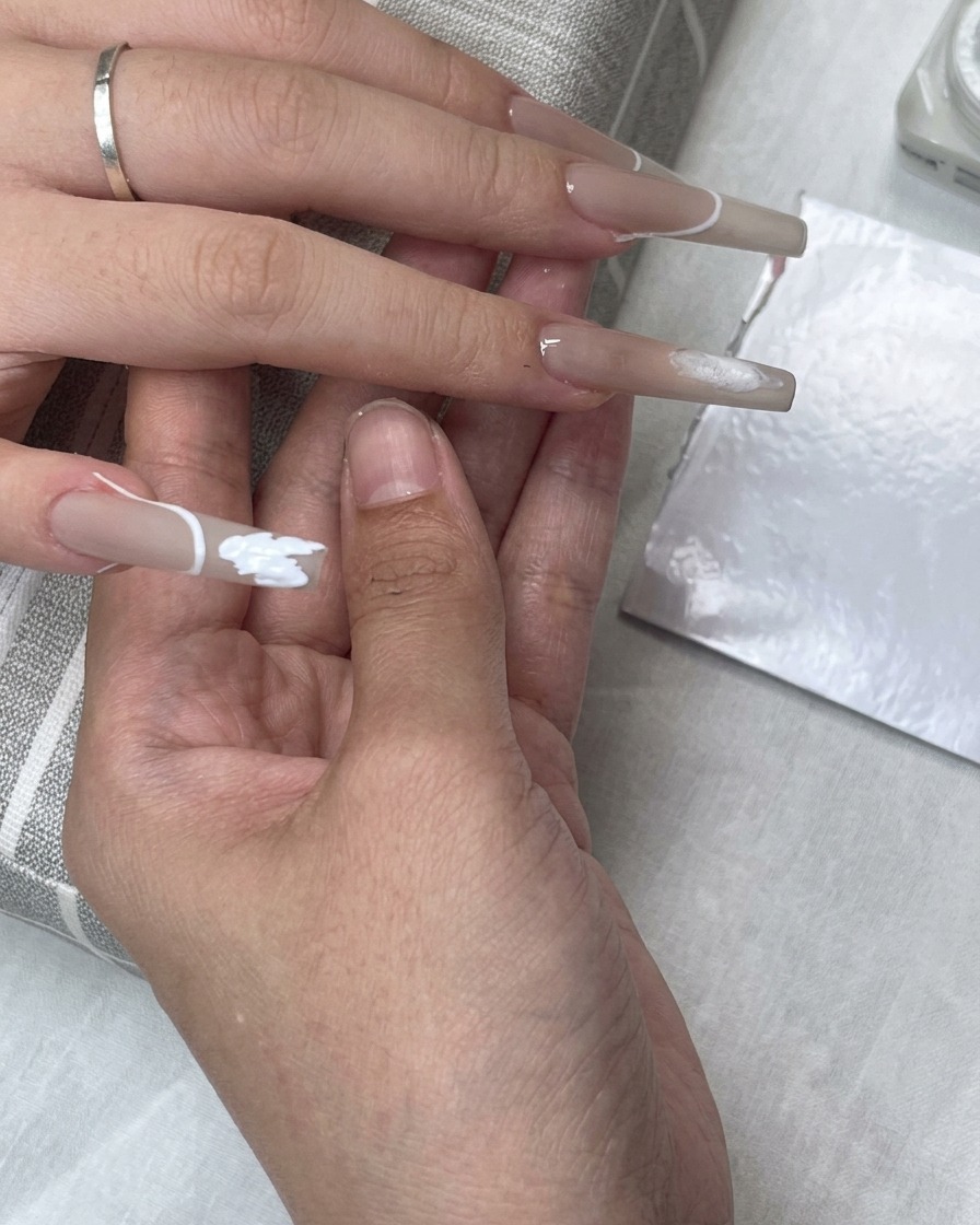 Un adesivo guida per French posizionato sullunghia mentre il gel bianco riempie larea della punta.