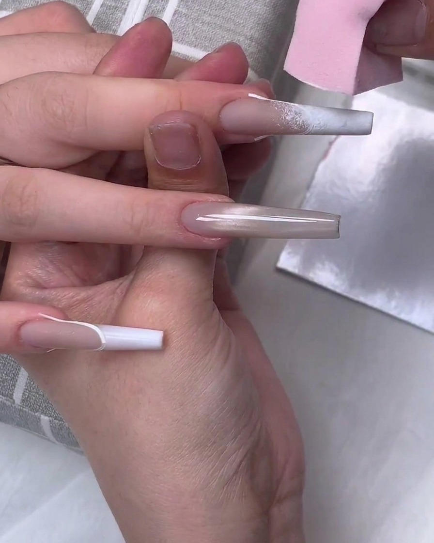 Una spugnetta rosa tampona lo smalto gel bianco sulla punta di ununghia lunga a ballerina per creare un effetto sfumato.