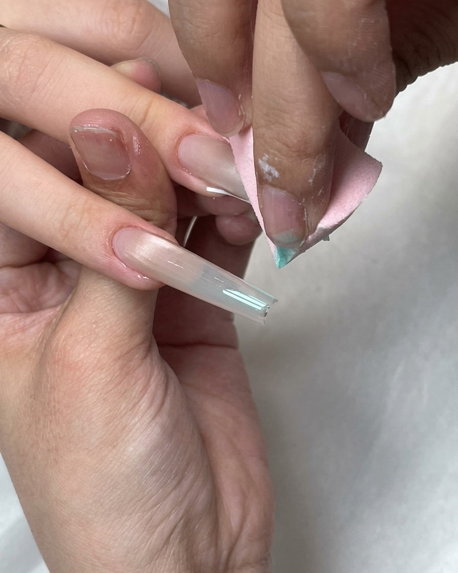 Una spugnetta rosa sfuma i puntini di gel blu sulla punta French bianca di ununghia lunga.