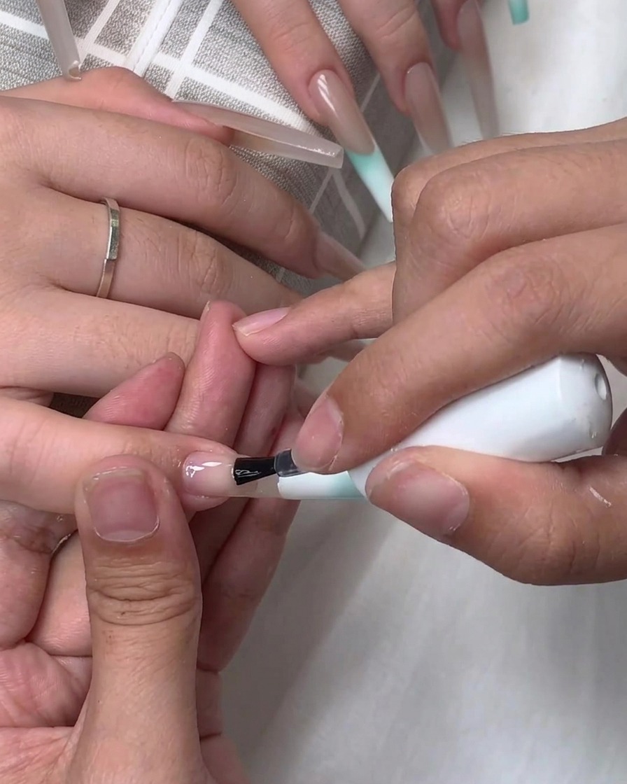 Un pennello applica la base trasparente o il top coat sulla superficie di ununghia allungata.