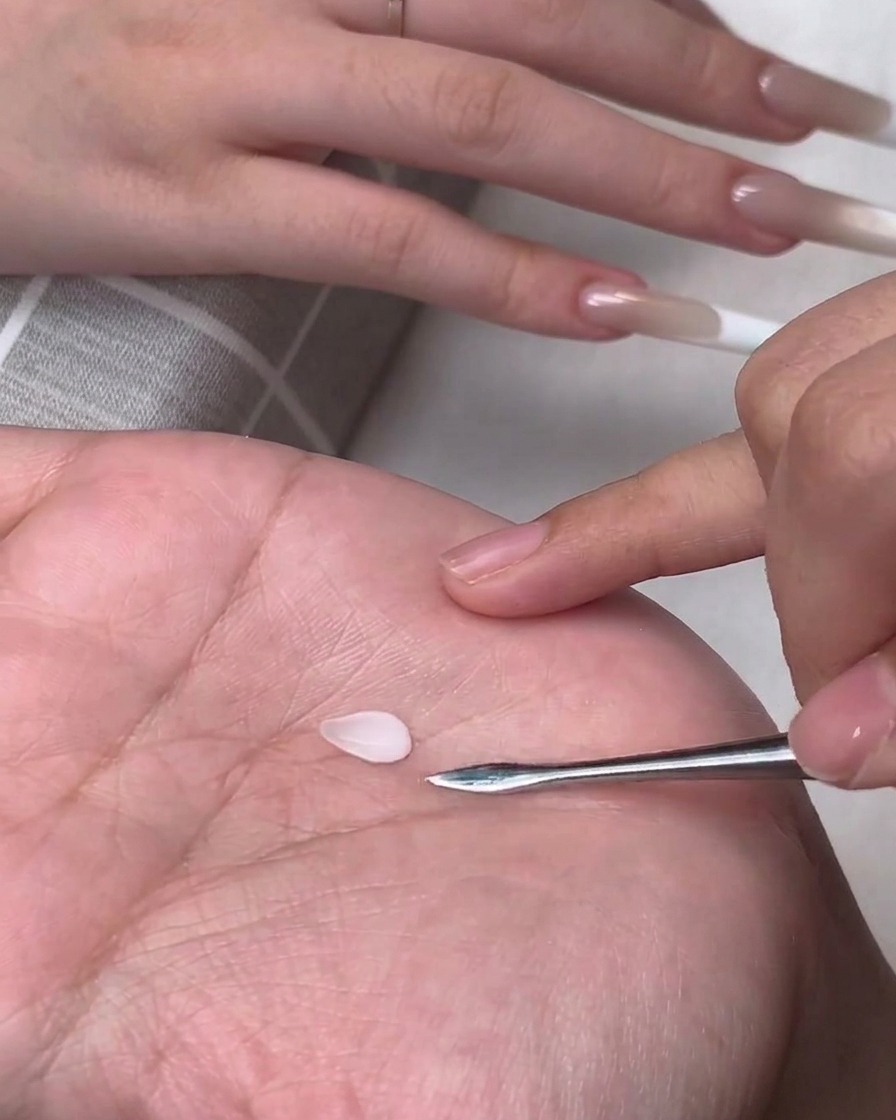 Un piccolo petalo di gel 3D bianco a forma di goccia poggiato sul palmo di una mano accanto a un attrezzo da scultura in metallo.