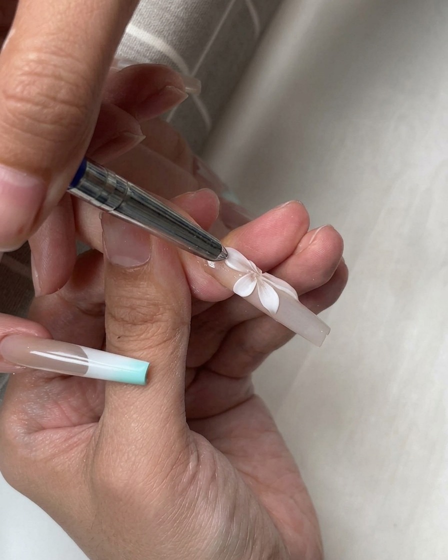 Uno strumento in silicone modella diversi petali bianchi 3D disposti a formare un fiore completo su ununghia.