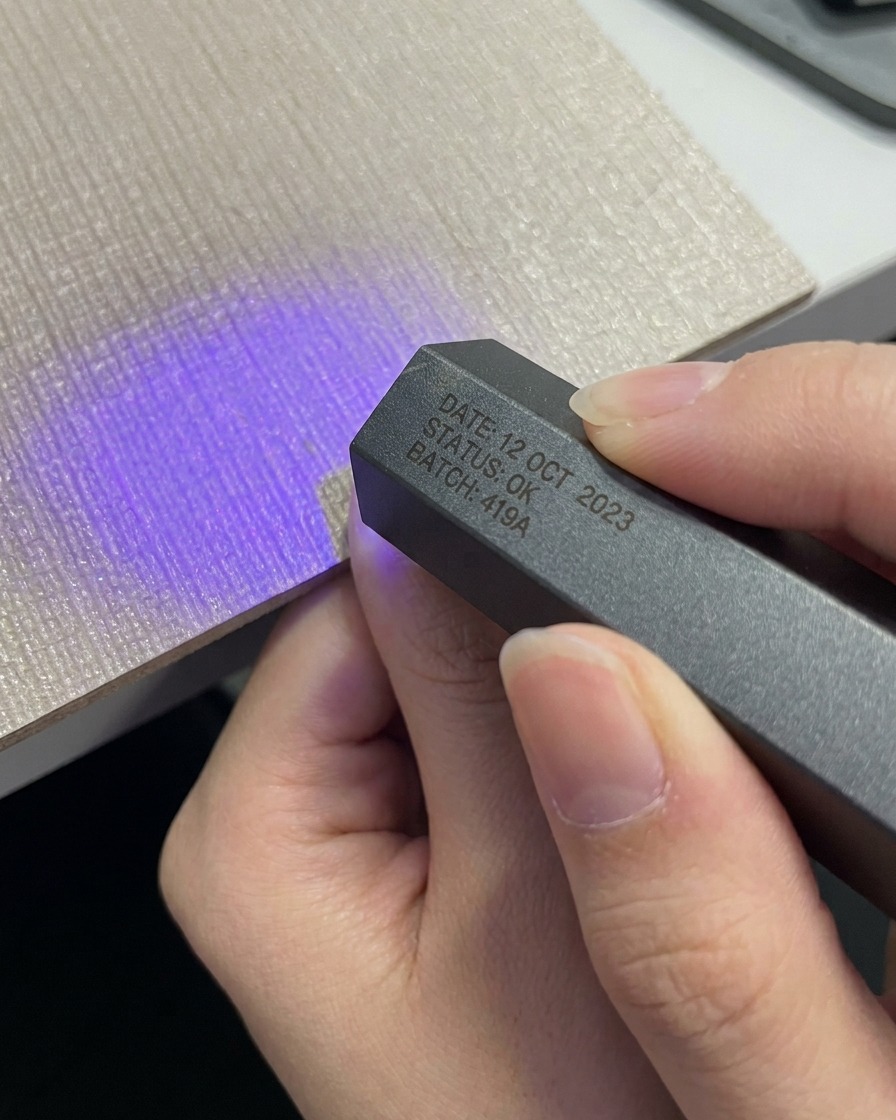 Una mano che posiziona un pollice sotto una mini lampada UV LED portatile grigia compatta.