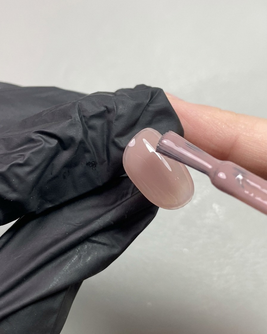 Un pennello che applica una seconda mano di gel nude trasparente dai toni aranciati su ununghia.