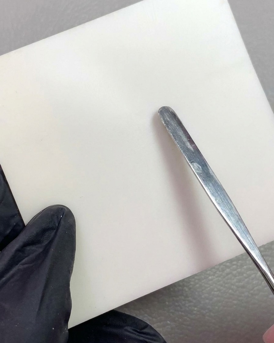 Uno strumento in metallo che posiziona un pezzo di gel da scultura bianco su una tavolozza di miscelazione pulita e bianca.