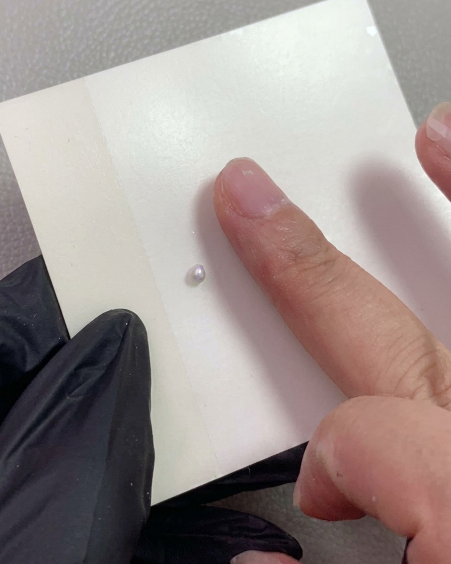 Una mano guantata che indica una piccola sfera di gel da scultura perla madreperla posizionata su un foglio da miscelazione.