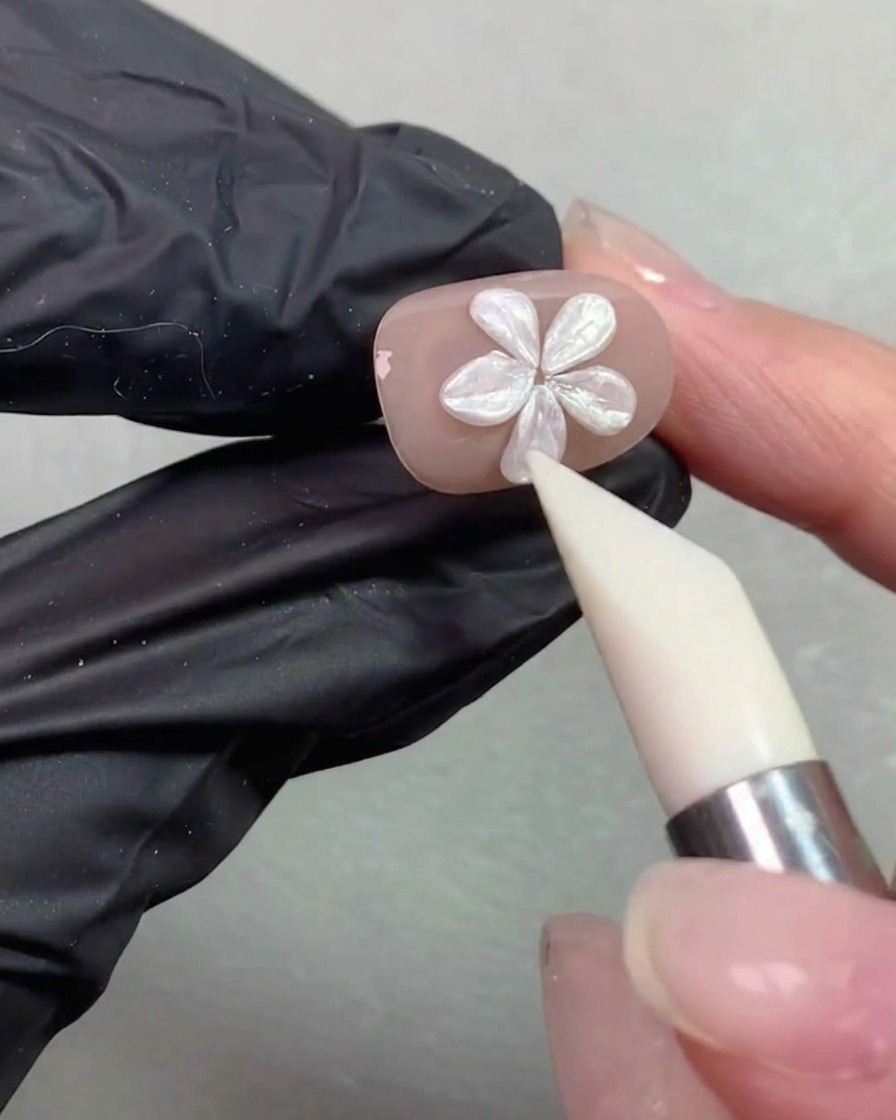 Una penna modellante in silicone che leviga e regola la forma dei petali di un fiore di perla su ununghia color nude.