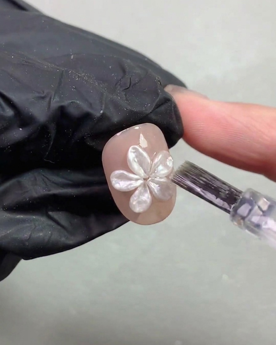 Un pennello da unghie che applica con cura un sottile strato di top coat attorno a un fiore di perla 3D polimerizzato su ununghia.