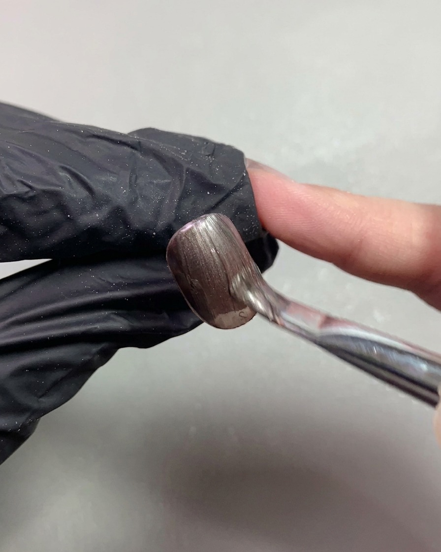 Un pennello che applica uniformemente il gel cat-eye magnetico marrone scuro su ununghia corta.