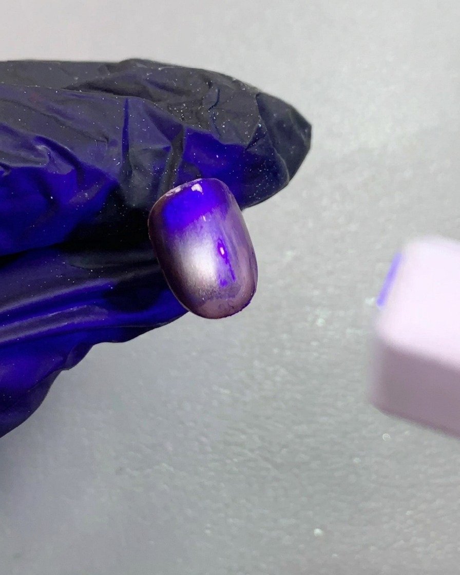 Vista ravvicinata di ununghia cat-eye magnetica marrone scuro in fase di polimerizzazione sotto una piccola lampada UV.