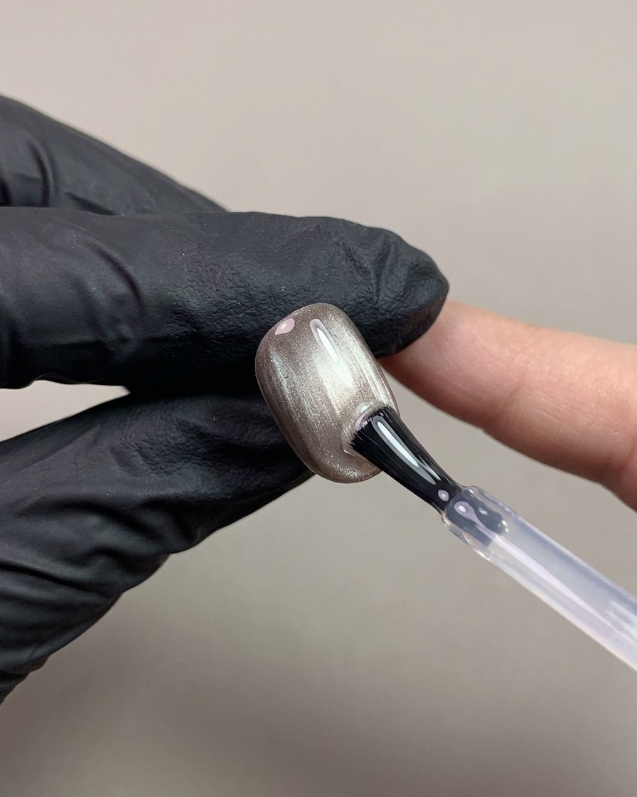 Un pennello per unghie che applica un top coat trasparente senza dispersione su ununghia cat-eye magnetica marrone scuro.