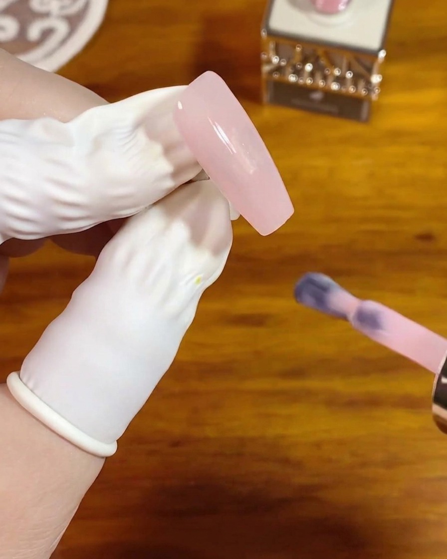 Un pennello per gel applica uno strato uniforme di gel rosa cristallo traslucido su una lunga unghia quadrata naturale.