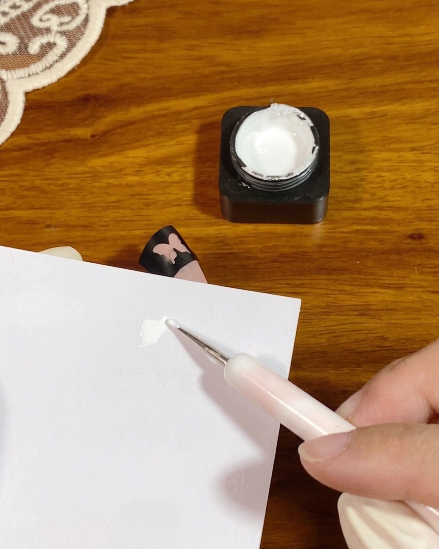Un dotting tool posiziona una piccola noce di gel bianco denso su un foglio di carta da tavolozza.
