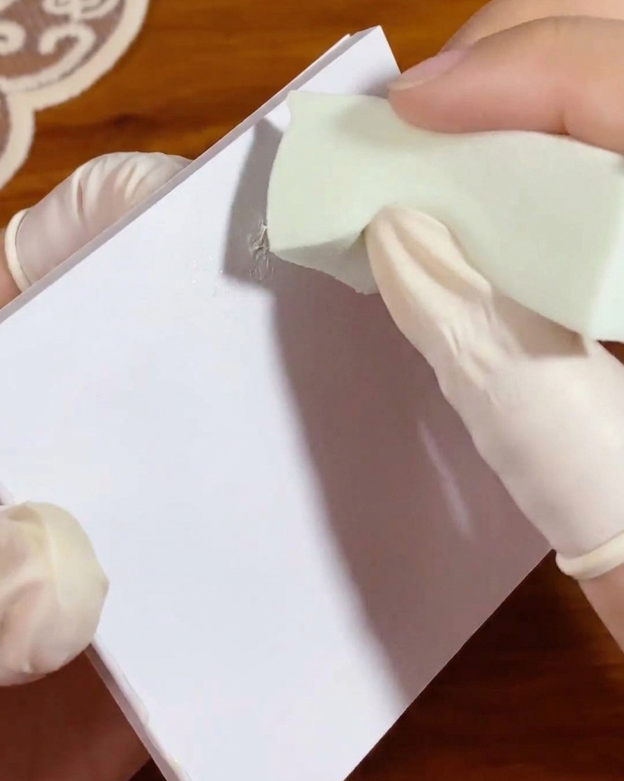 Una piccola spugnetta da trucco verde viene tamponata su una macchia di gel bianco su una carta da tavolozza per distribuire uniformemente il colore.