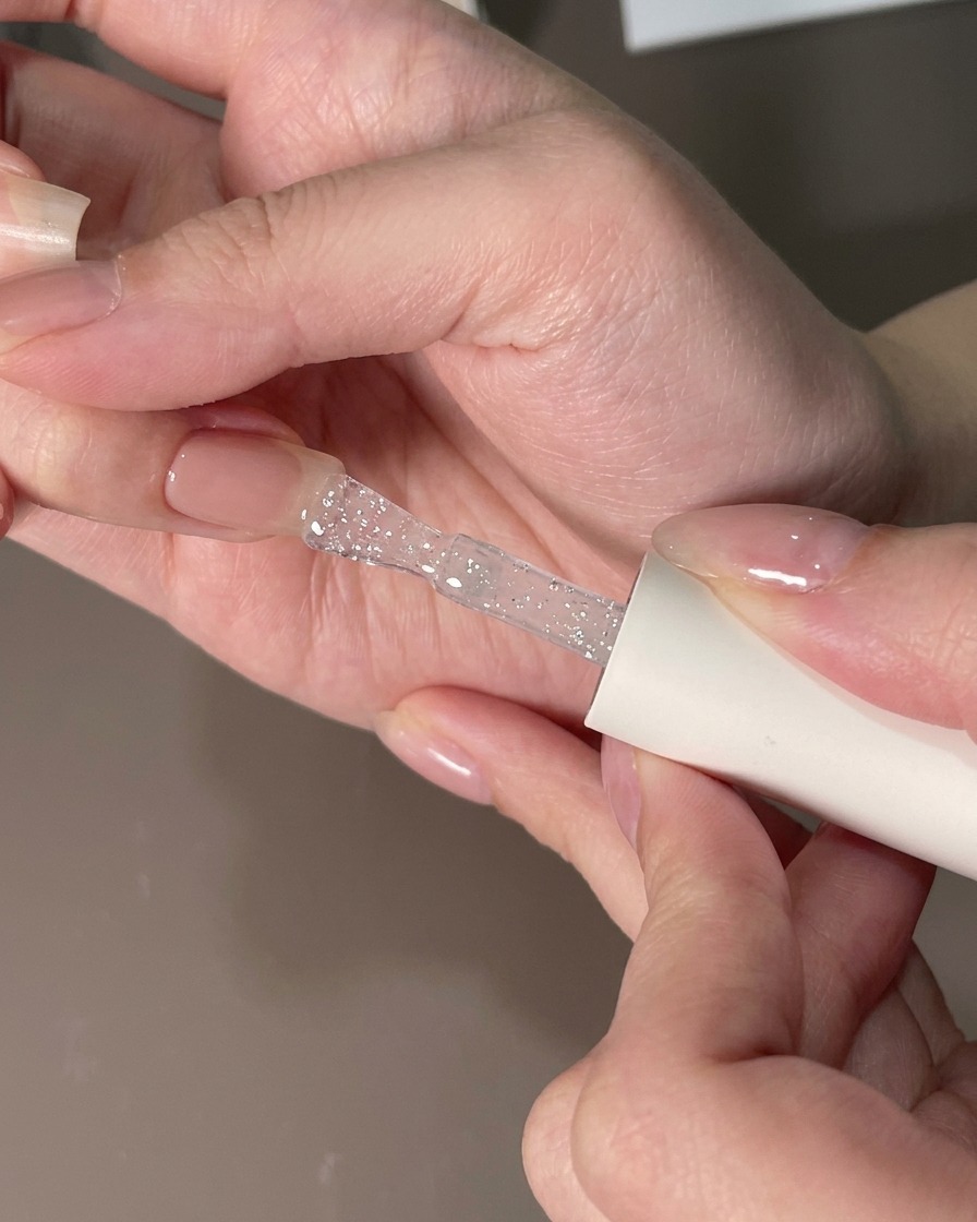 Un pennello piatto che livella uno strato di gel trasparente su ununghia per rimuovere le particelle.