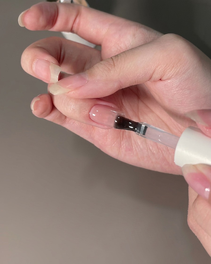 Un pennello che applica un top coat sigillante su ununghia rifinita con polvere cromata.