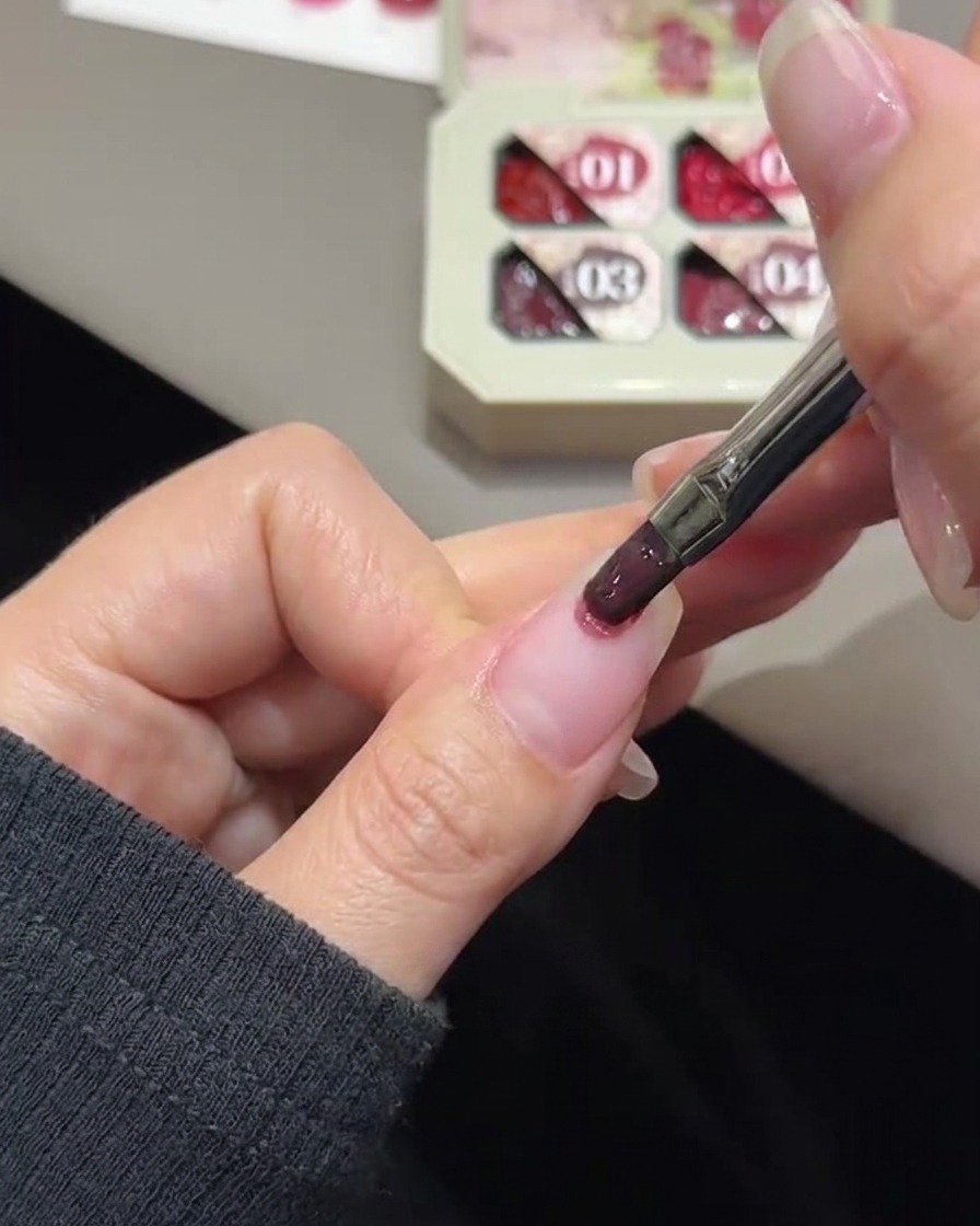 Un pennello da unghie che tampona il gel color rosa sulla punta di ununghia naturale.