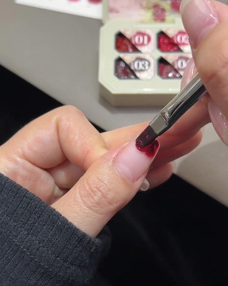 Una piccola spugnetta bianca da trucco a cuneo che sfuma il colore del gel rosa sulla punta di ununghia.
