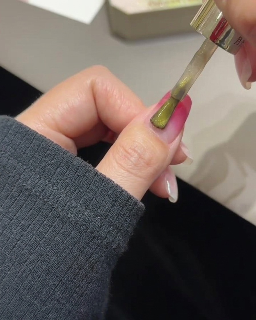 Un pennello che applica il gel cat eye dorato su ununghia con sfumatura rosa polimerizzata.