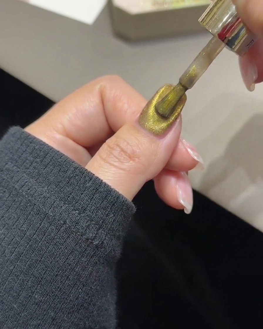 Uno strumento a bacchetta magnetica che si libra sopra ununghia per concentrare le particelle magnetiche dorate in una fascia di luce.
