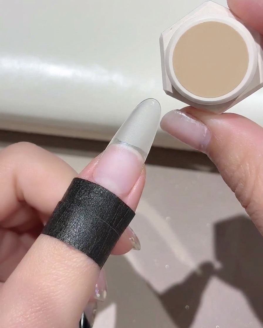 Una piccola spugna che tampona un colore gel nude su una tip per unghie finte trasparenti.