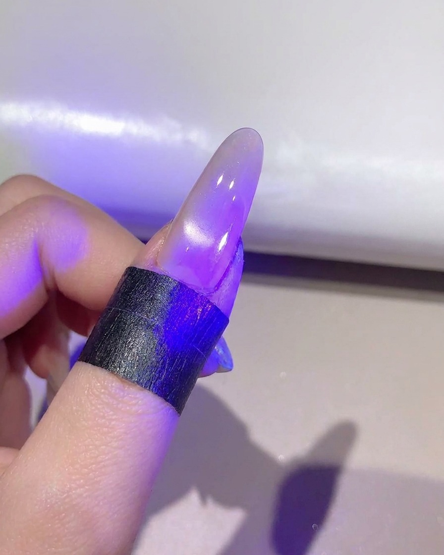 Ununghia sotto una lampada UV/LED viola che polimerizza lo strato di gel cat-eye finito.