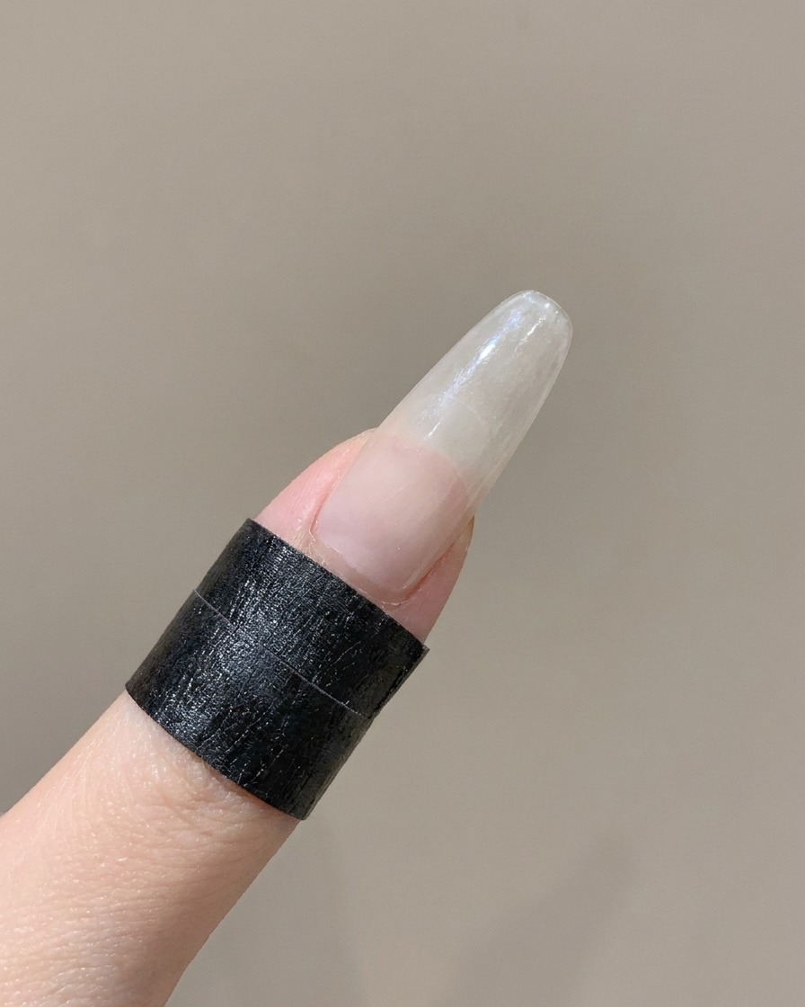 Uno strumento in silicone che preme il bordo curvo di un adesivo per unghie French su un dito.