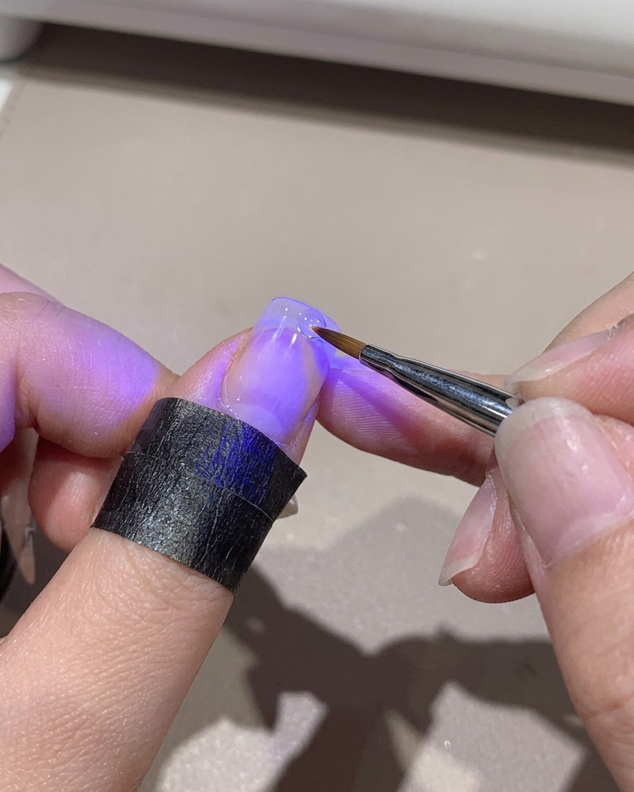 Una mini lampada UV che polimerizza la punta di ununghia sfumata mentre viene tenuta a mano.